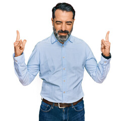 Naklejka premium Middle aged man with beard wearing business shirt shouting with crazy expression doing rock symbol with hands up. music star. heavy music concept.