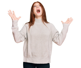 Young read head woman wearing casual winter sweater crazy and mad shouting and yelling with aggressive expression and arms raised. frustration concept.