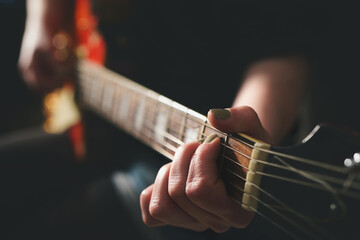 Dark scenery with woman playing chord on electric guitar. selective focus on part of left hand with...