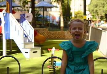 A funny girl with a sly look. Preschool girl portrait of a cheerful girl in a green dress with two pigtails.