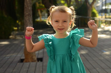 A funny girl with a sly look. Preschool girl portrait of a cheerful girl in a green dress with two...