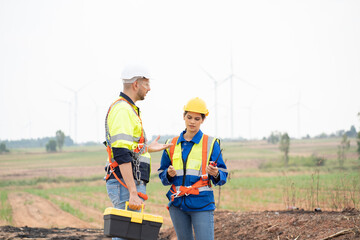 Male and female engineer working at wind turbines farm, discussing and inspecting quality wind turbines, planing maintenance of wind turbines at windmill field farm