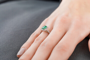 Beautiful female hand with gold ring with diamonds and emerald on gray background