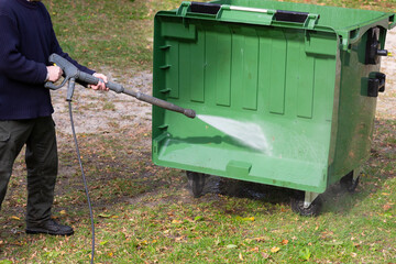 A municipal service worker treats a garbage container with a disinfectant solution. Washing the garbage container.	