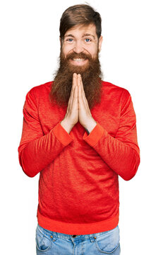 Redhead man with long beard wearing casual clothes praying with hands together asking for forgiveness smiling confident.