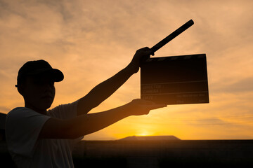 Teenage boy holding a film slate or film clapper board at sunset. new content creator, young...
