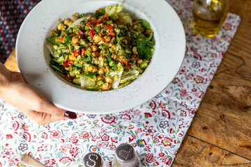 Woman in yellow t-shirt and navy blue nail polish holding a red cocktail garnished with basil