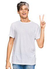 Young hispanic man wearing casual white tshirt smiling with happy face winking at the camera doing...