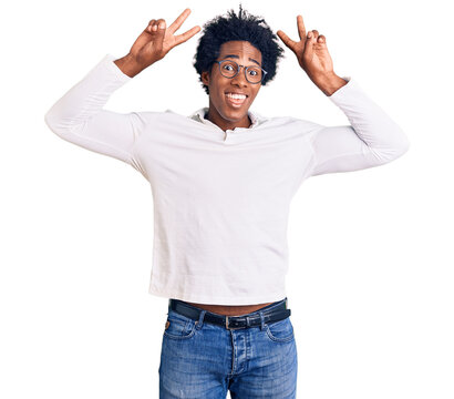 Handsome african american man with afro hair wearing casual clothes and glasses posing funny and crazy with fingers on head as bunny ears, smiling cheerful