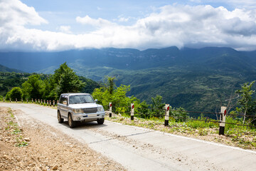 4x4 off-road car driving on a gravel road uphill towards Khvamli Mountain peak in lush green Tskhenistsqali valley in Racha region in Georgia.