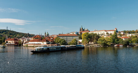 Fototapeta na wymiar A boat is sailing on a river with a cityscape in the background. Pleasure boat on the Vltava pier in the fall. View of Prague.