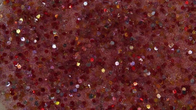 Multicolored particles like confetti or spangles float in a viscous liquid and glitter in the light with depth of field. Glitter texture. Particles background. Shining sparkles. Cosmetics concept.