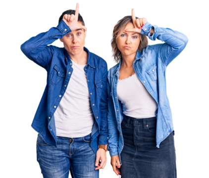 Couple of women wearing casual clothes making fun of people with fingers on forehead doing loser gesture mocking and insulting.