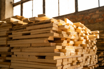Stacked raw wooden planks at a indoor lumber warehouse. Background of boards. Raw wood drying in the lumber warehouse. Wood industry.