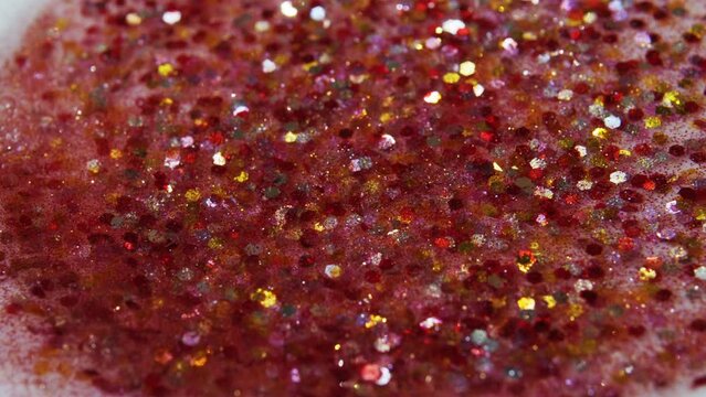 Multicolored particles like confetti or spangles float in a viscous liquid and glitter in the light with depth of field. Glitter texture. Particles background. Shining sparkles. Cosmetics concept.
