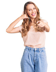 Young beautiful caucasian woman with blond hair wearing casual clothes smiling doing talking on the telephone gesture and pointing to you. call me.