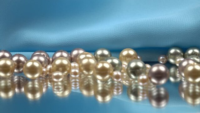 Pearl beads of various colors lie on the mirror and are reflected in it against the background of blue satin fabric