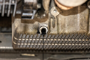 Changing old motor oil in automobile repair service. maintenance and checkup in car workshop. Auto is on hydraulic lift in garage workshop, process of draining old dark used oil. Engine oil change