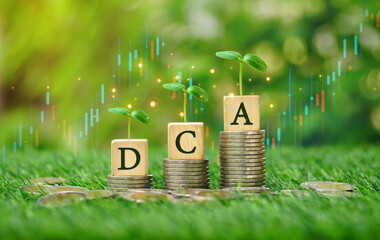 Rows of money coins stacks with DCA word on wooden cube and growing tree on top and candlestick...