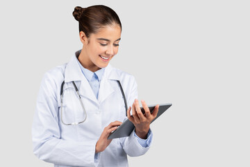 Smiling young european woman professional doctor or intern typing on tablet chatting