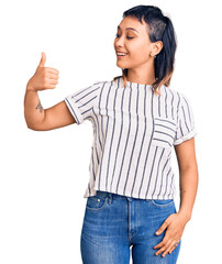 Young woman wearing casual clothes looking proud, smiling doing thumbs up gesture to the side