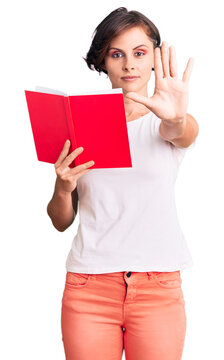 Beautiful young woman with short hair reading a book with open hand doing stop sign with serious and confident expression, defense gesture