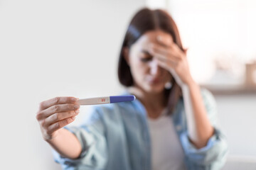 Upset lady holding positive pregnancy test at home, covering face