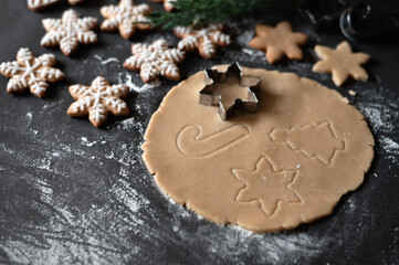 Obraz na płótnie Canvas Rolled dough on table with snowflake, Christmas tree and cane ornaments of cookie cutters, baked snowflake cookie on black table background with flour. Soft selective focus, lifestyle