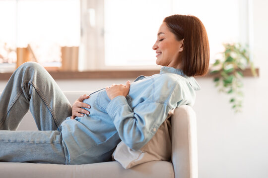 Pregnant Young Woman Hugging Belly Resting On Sofa At Home