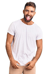 Young hispanic man wearing casual white tshirt sticking tongue out happy with funny expression. emotion concept.