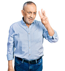 Senior man with grey hair and beard wearing casual blue shirt showing and pointing up with fingers number three while smiling confident and happy.