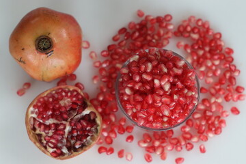 Vibrant pomegranate fruit and red pearl like arils glisten in a glass bowl, showcasing freshness...