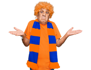 Senior hispanic man football hooligan cheering game clueless and confused expression with arms and hands raised. doubt concept.