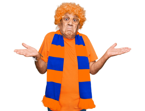 Senior hispanic man football hooligan cheering game clueless and confused expression with arms and hands raised. doubt concept.