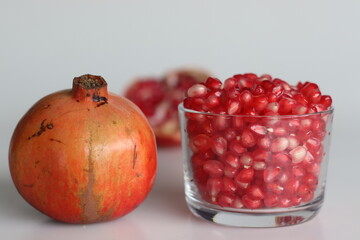 Vibrant pomegranate fruit and red pearl like arils glisten in a glass bowl, showcasing freshness and juicy allure