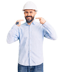 Young handsome man wearing architect hardhat smiling cheerful showing and pointing with fingers teeth and mouth. dental health concept.