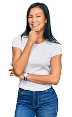 Beautiful hispanic woman wearing casual white tshirt looking confident at the camera smiling with crossed arms and hand raised on chin. thinking positive.