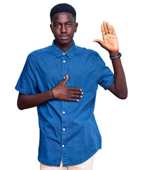 Young african american man wearing casual clothes swearing with hand on chest and open palm, making...