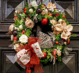 Adorn your entrance door with a festive tapestry of evergreen garlands intertwined with twinkling fairy lights, creating a warm ambiance, a symphony of rich red ribbons and glistening ornaments.