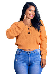 Hispanic woman with long hair wearing casual winter sweater doing happy thumbs up gesture with...