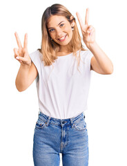 Fototapeta na wymiar Beautiful caucasian woman with blonde hair wearing casual white tshirt smiling looking to the camera showing fingers doing victory sign. number two.