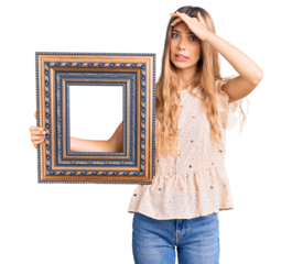Beautiful caucasian woman with blonde hair holding empty frame stressed and frustrated with hand on head, surprised and angry face