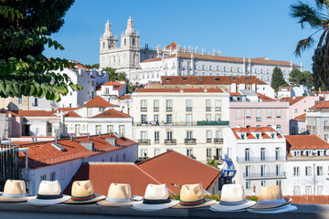 Close up of several typical Portuguese straw hats displayed on a wall in Alfama neighborhood, Lisbon, Portugal with colorful houses and Monastery of São Vicente de Fora in background - obrazy, fototapety, plakaty