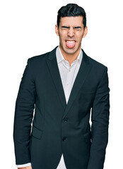 Handsome hispanic man wearing business clothes sticking tongue out happy with funny expression. emotion concept.