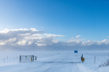 View over snowy landscape and snow covered road with cattle grid in Iceland with high winds blowing...