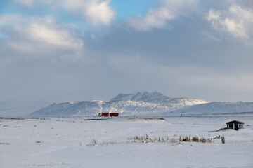 Panoramic view over snow covered landscape with snow covered mountains in skimming winter sunlight in background on Iceland with bright red truck as contrast on road in distance