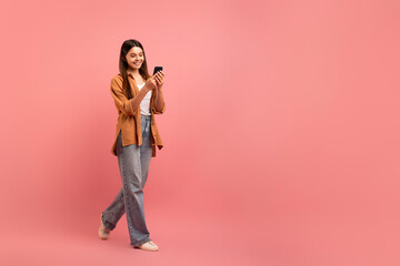 Mobile Communication. Smiling Teen Girl Walking With Smartphone Over Pink Background