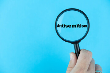 Global rise of Antisemitism concept, depicted through a magnifying glass focusing on the word...