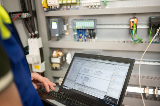 Programmer of PLC checks correct function of program in PLC with electrical cabinet in background