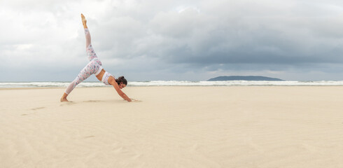 Wide panoramic shot of Young beautiful slender woman doing yoga on the sand beach.